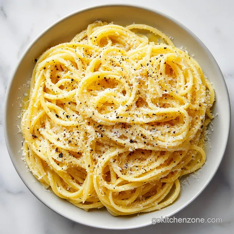 Swirls of buttered pasta topped with a snow-like dusting of parmesan and herbs on a minimalist matte black plate.